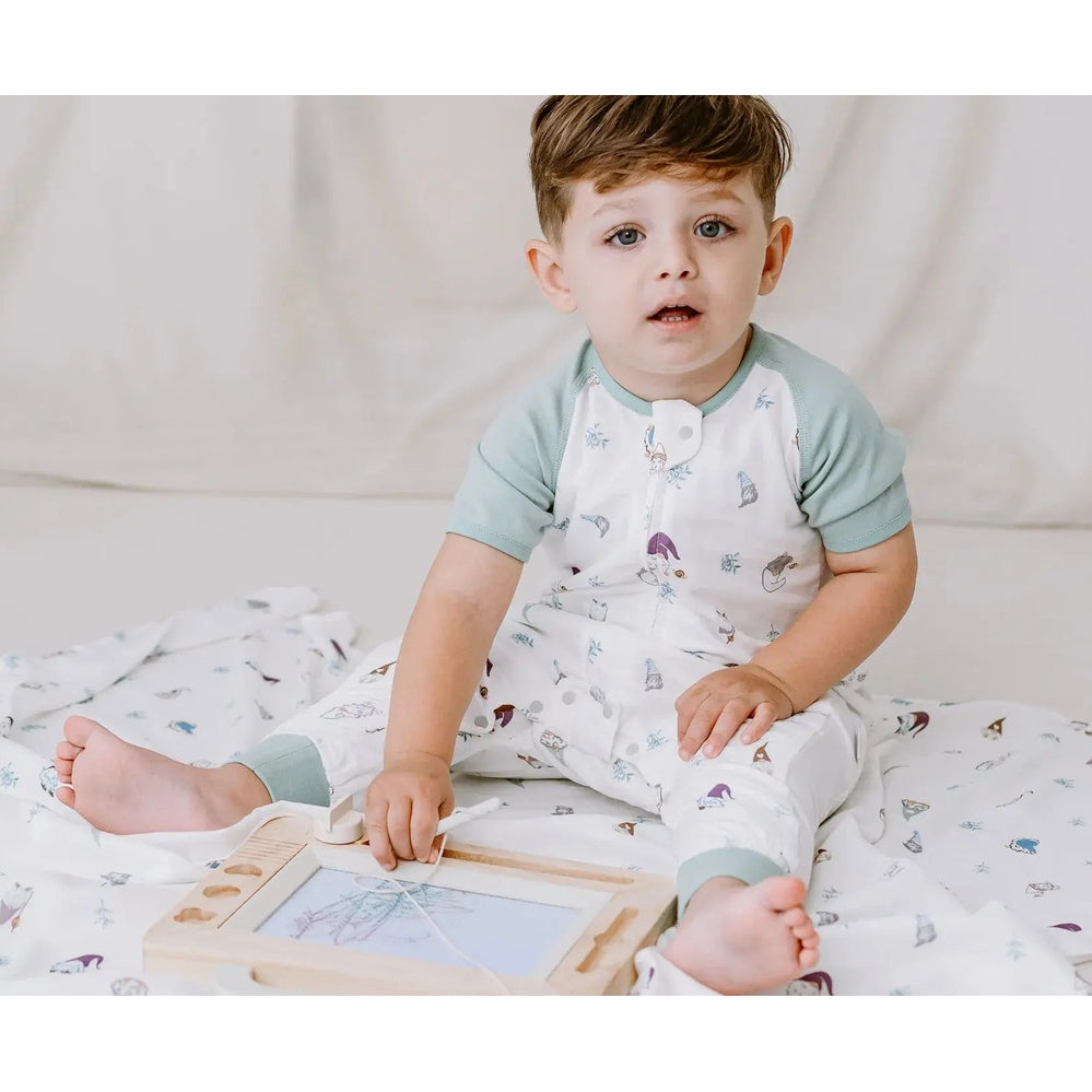 Nest Designs bamboo Pima sleep bag 0.6 Tog with gnome print, toddler sitting on bed playing with a wooden toy.