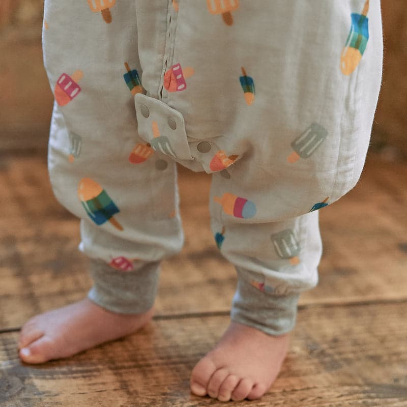 Nest Designs Raglan Bamboo Pima Short Sleeve Footed Sleep Bag 0.6 Tog Summer Pops; baby stands barefoot in the printed sleepsack.