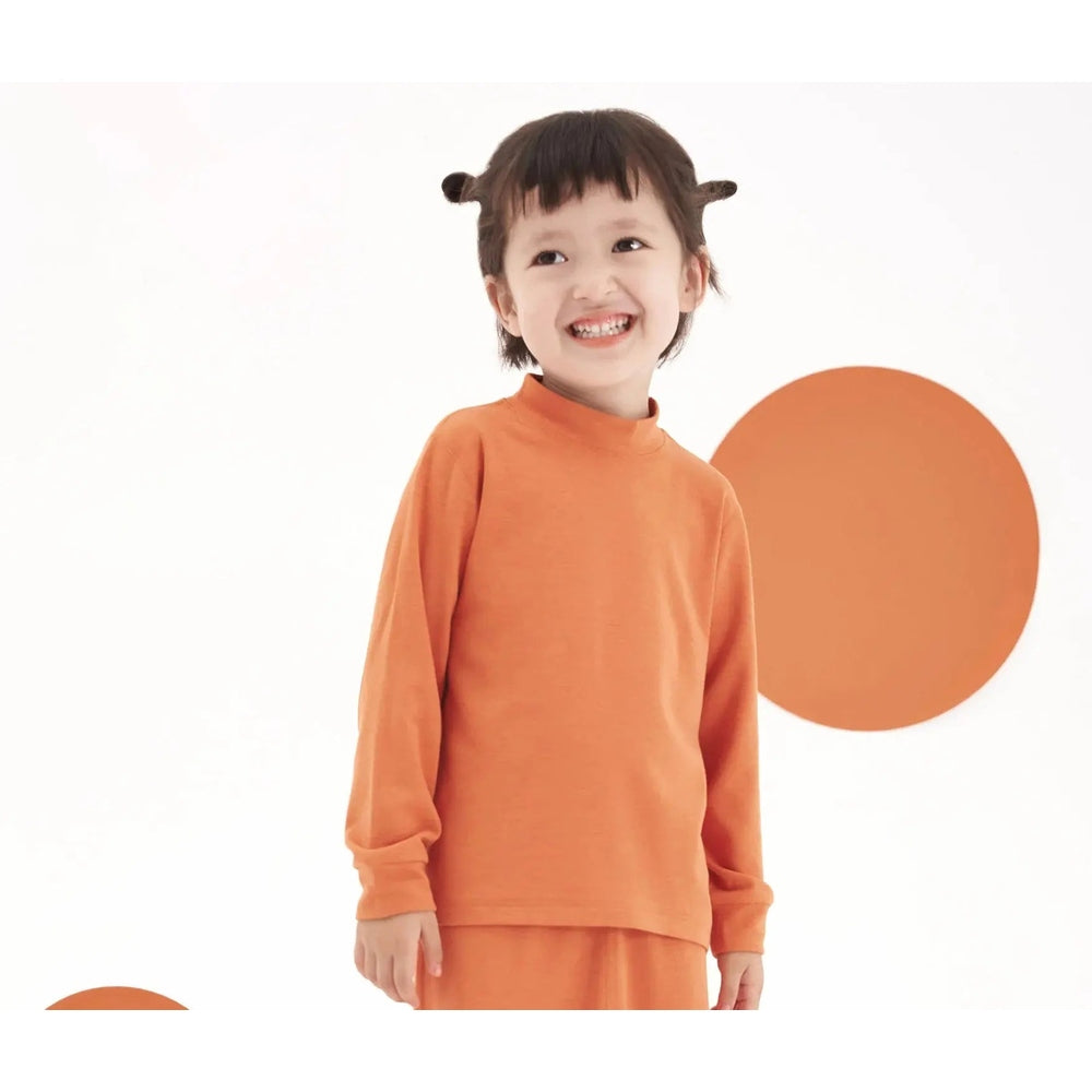 Nest Designs Tanboocel mock-neck long-sleeve shirt and pants in apricot orange; toddler stands smiling, showcasing cozy matching set.