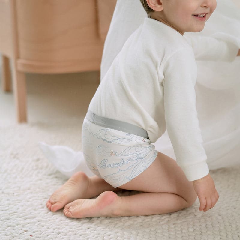 Nest Designs Bamboo Boys Boxer Briefs Underwear (2 Pack) Surf Camp; toddler kneels on carpet wearing light blue wave-print briefs.