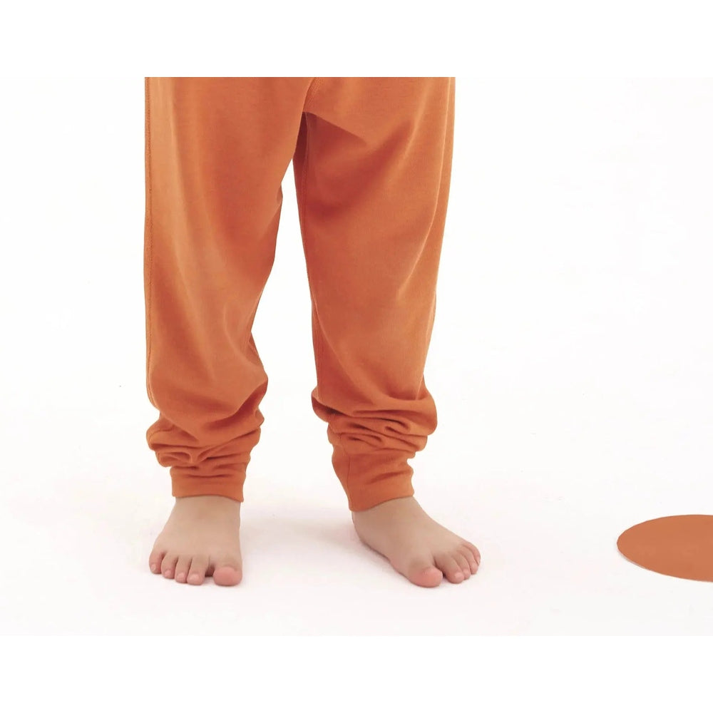 Nest Designs Tanboocel Pants Pantone Apricot Orange baby jogger pants with cuffed ankles, child standing barefoot.