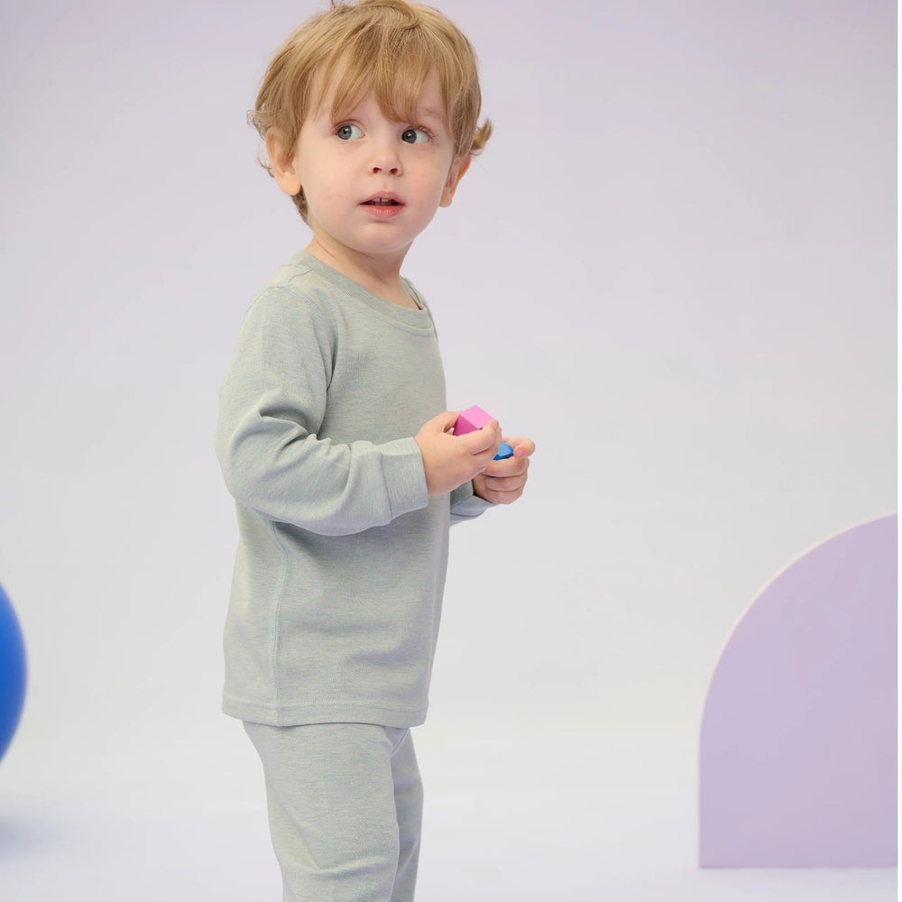 Nest Designs Tanboocel two-piece slate long-sleeve PJ set for toddlers; child holds pink and blue blocks.