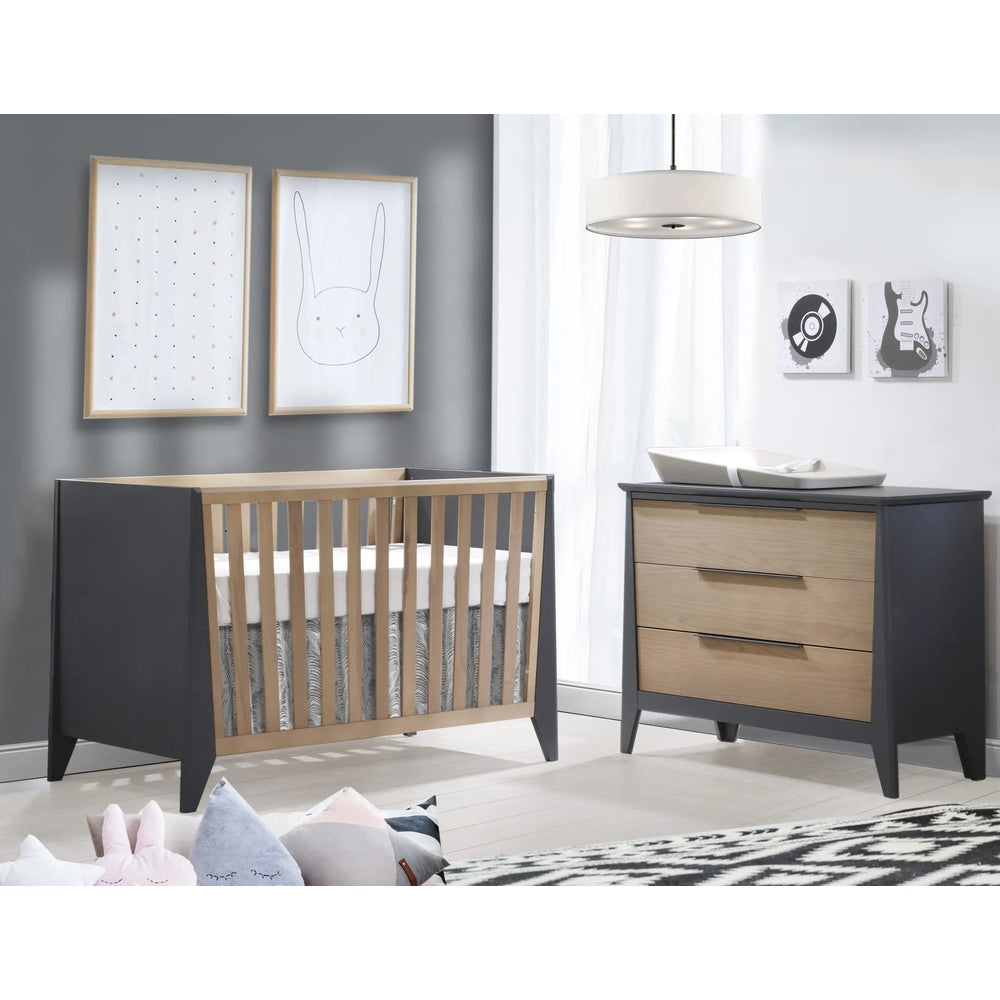 Nest Flexx Premium Classic Crib in natural birch with dark gray end panels beside a matching dresser in a bright nursery.