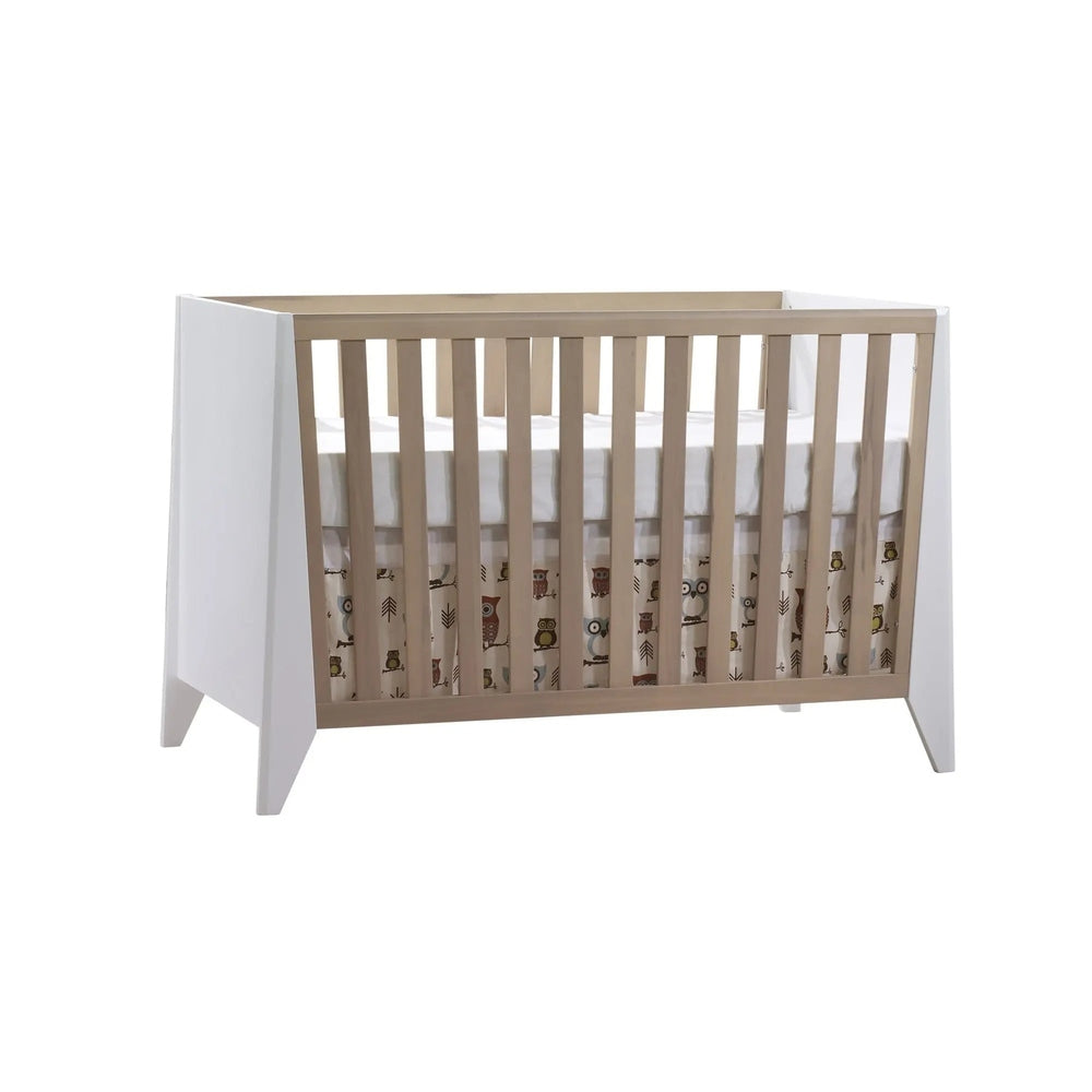 Nest Flexx Premium Classic Crib in natural birch with white end panels and slatted sides, shown with a fitted mattress and owl-printed skirt.