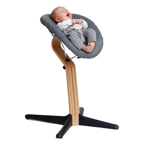 NOMI Baby high chair with gray cushion and wooden frame; baby reclines and smiles.
