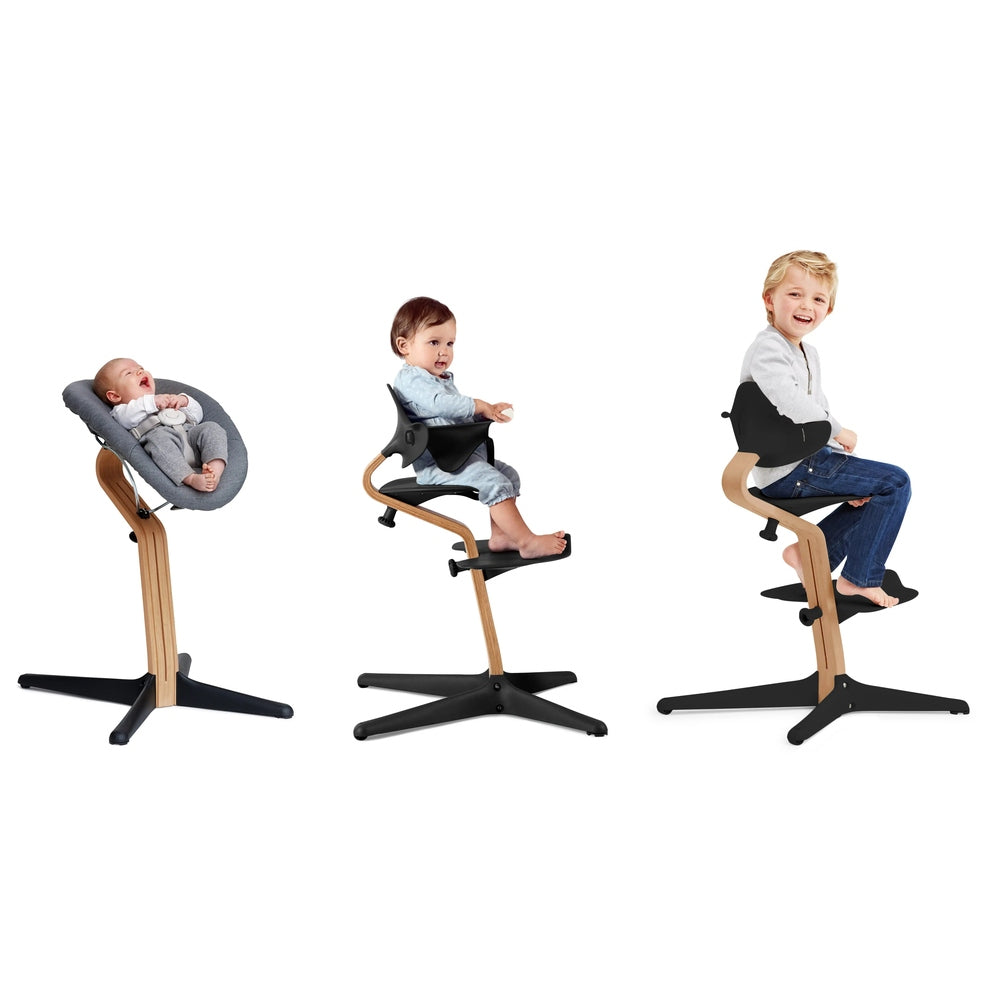 Nomi Chair White Oak high chair shown in three ages: infant in gray pad, toddler in black seat, child on wood frame with black base.
