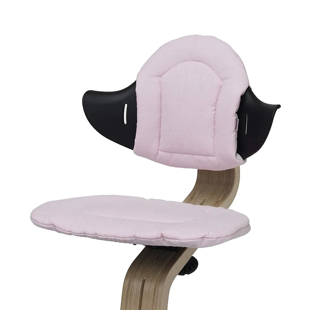 NOMI Highchair Cushion in light pink fabric with black winged headrest, attached to a wooden chair.