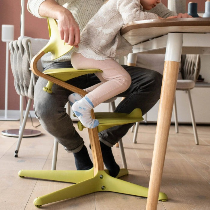 NOMI Highchair White Oak with lime-green frame; a toddler sits at the table for mealtime.