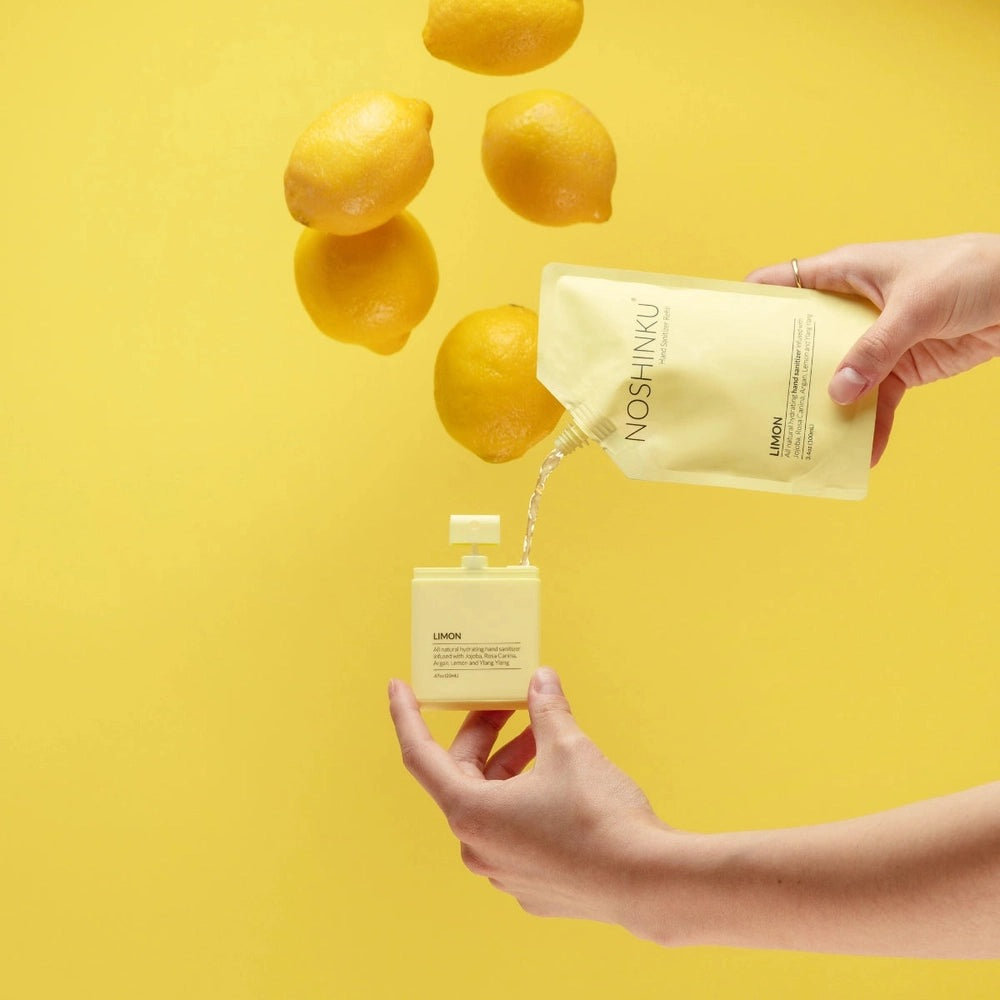 NOSHINKU hand moisturizer refill pouch pouring into a white dispenser bottle against a bright yellow background with floating lemons