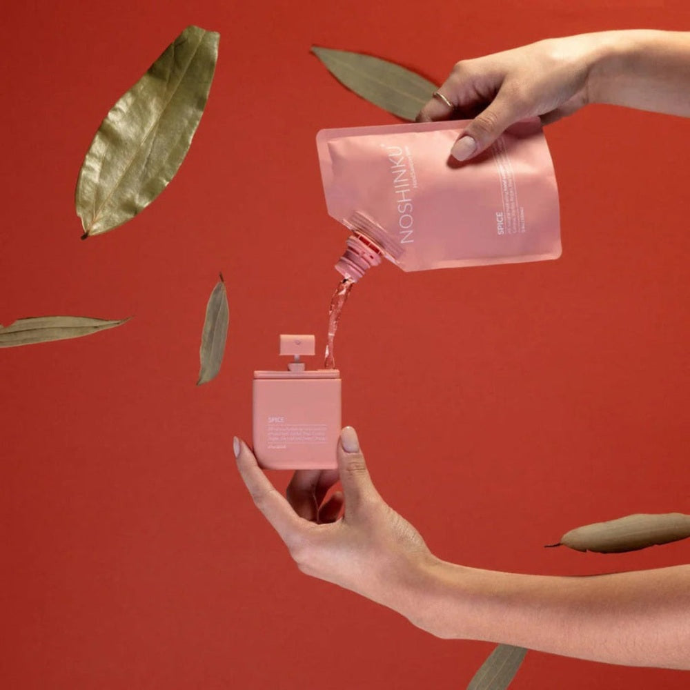 NOSHINKU Hand Moisturizing Refill Pouch 3.4 oz pours pink lotion into a matching bottle against a warm coral backdrop.