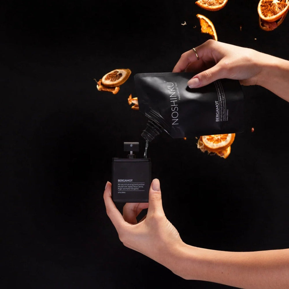 NOSHINKU Refillable Moisturizing Pocket Hand Sanitizer pouch pours into a small pump bottle amid orange slices.