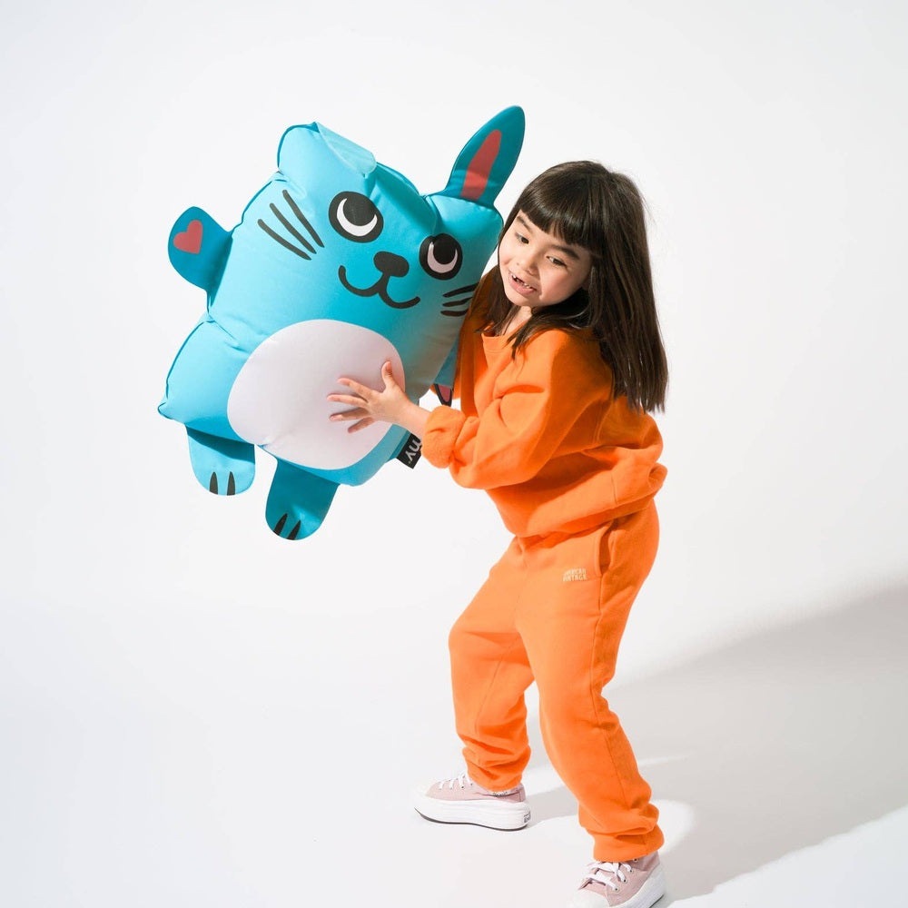 OMY Bunny Super inflatable pillow; a girl in orange hugs the large blue inflatable pillow, playful party decor.
