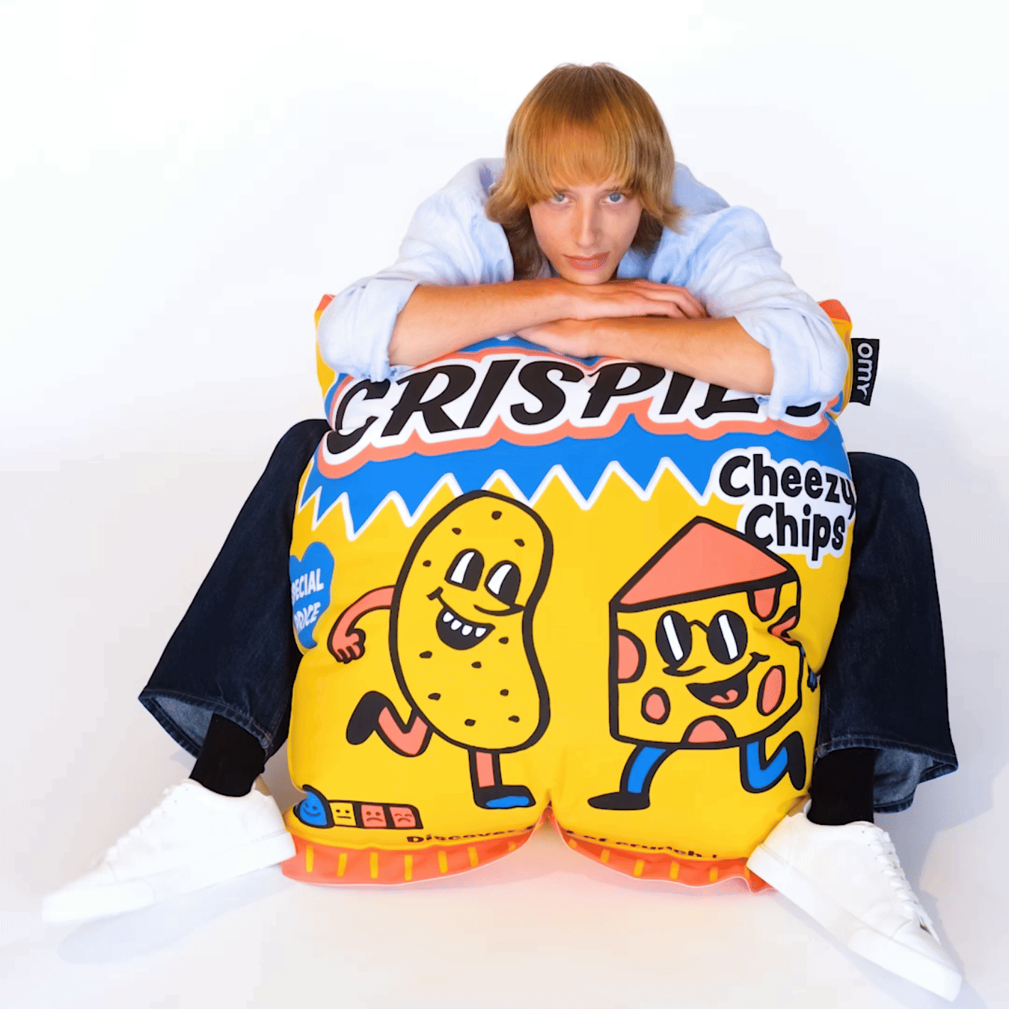 OMY Crispies Giant inflatable pillow, with cartoon peanut and cheese characters, as a person leans on it.