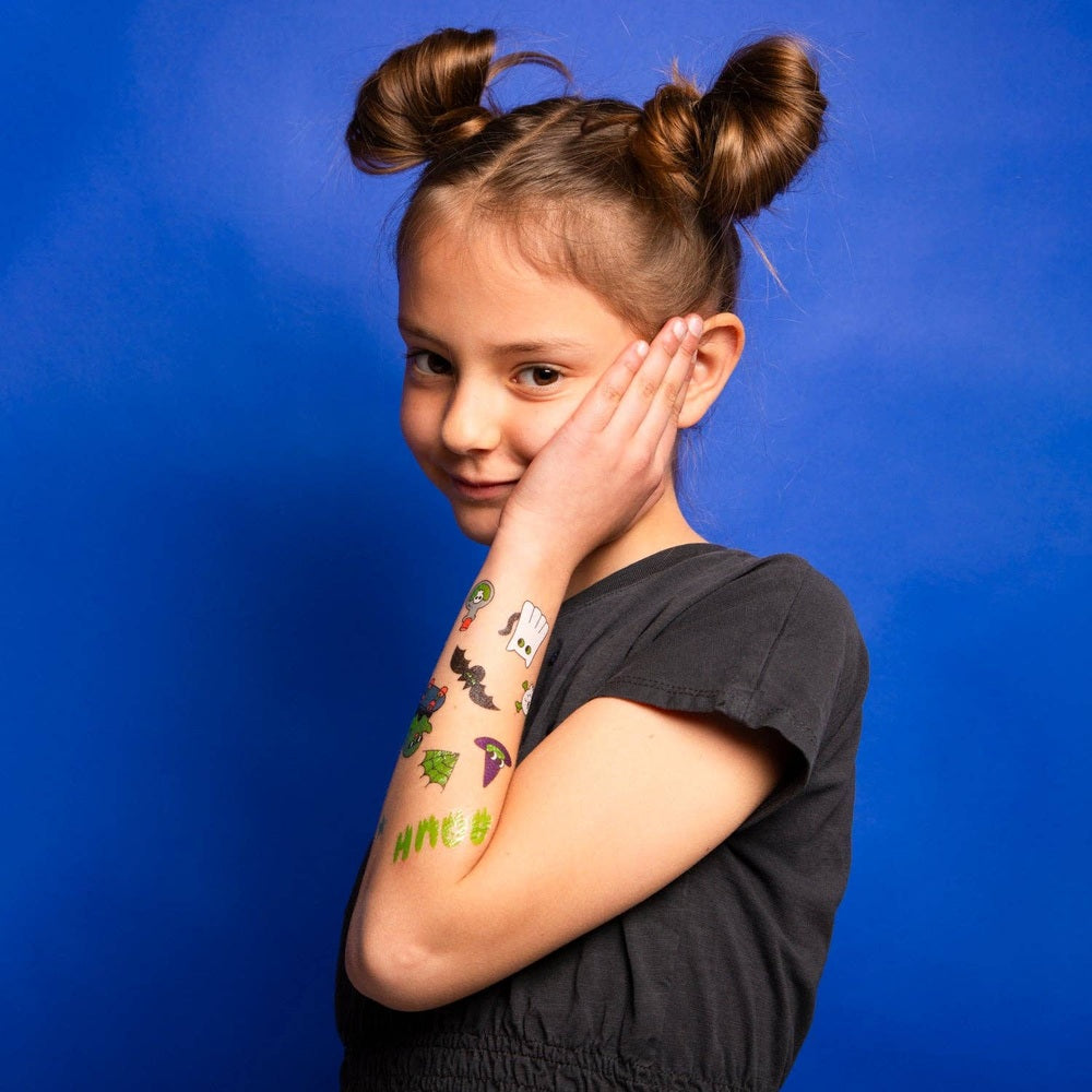 OMY Glow in the Dark Tattoos on a girl's forearm, colorful designs shown as she smiles against a blue backdrop