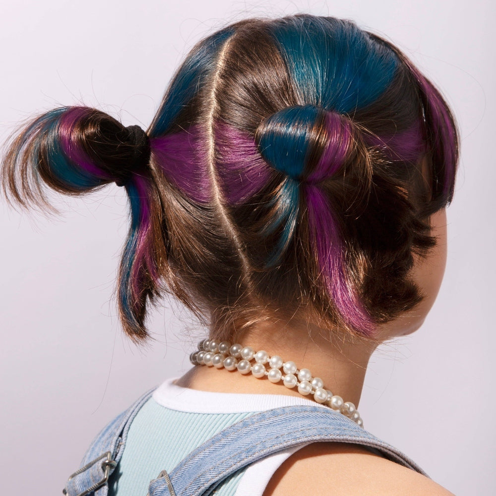 OMY Hair Chalk on brunette with blue, purple and pink highlights in twin buns, pearl necklace visible.