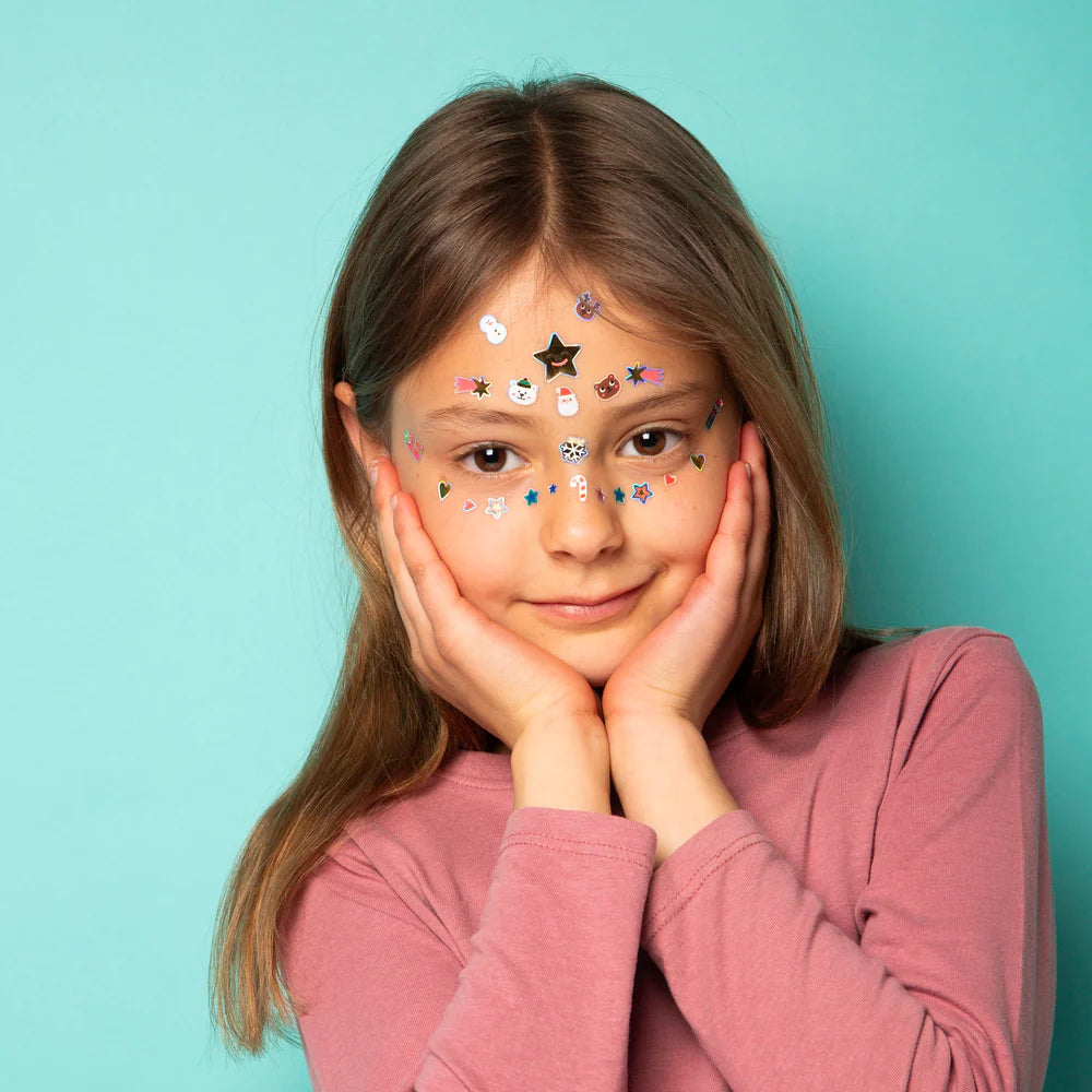 OMY Hohoho Holiday! Face stickers on a smiling girl, colorful festive stickers on her forehead and cheeks.