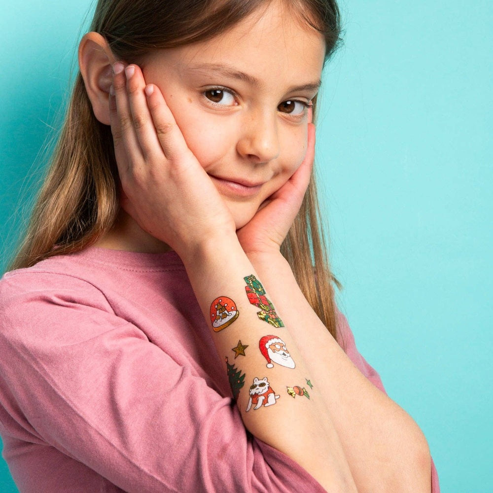 OMY Hohoho Holiday! temporary tattoos on a girl's forearm, festive Santa and tree designs shown.