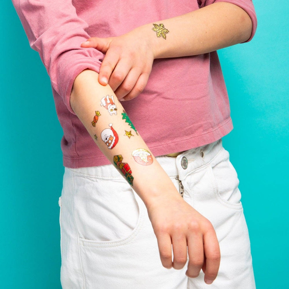 OMY Hohoho Holiday! temporary tattoos on a child's forearm being applied with festive designs.