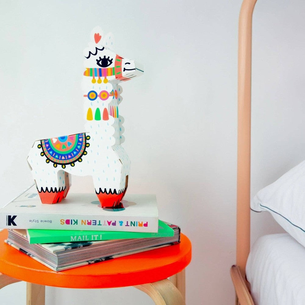 OMY Lama 3D Lamp, white decorative llama with bright patterns perched on books on an orange bedside table.