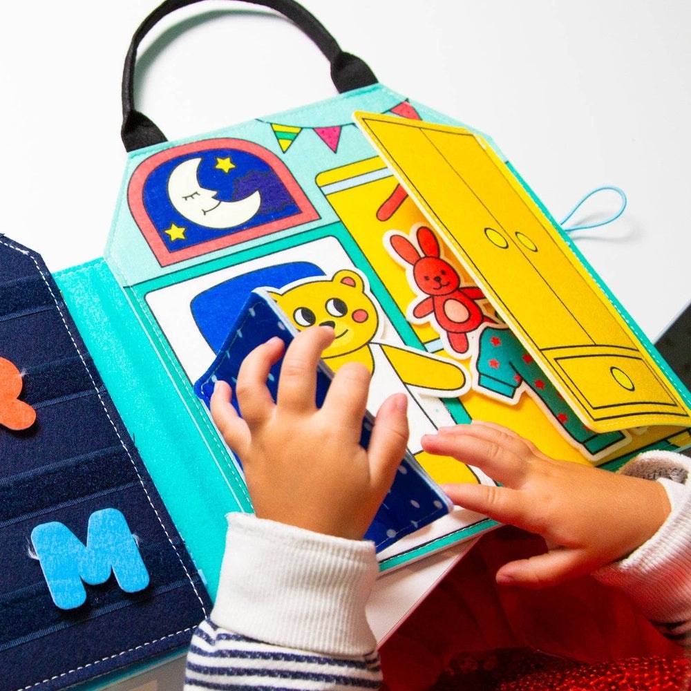 OMY Montessori Play Kit open on a table as a child touches a blue card among colorful learning panels.