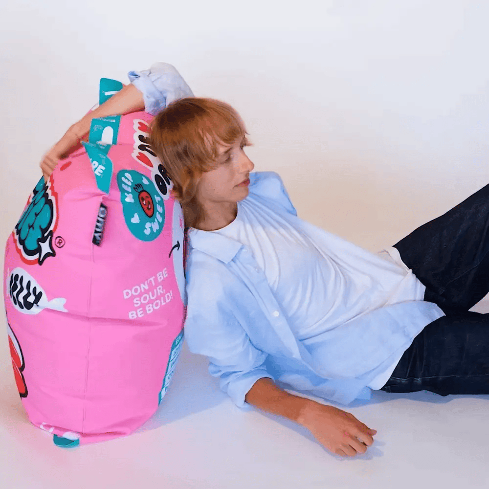 OMY Strawbies Giant inflatable pillow in pink; person leans back against the oversized colorful cushion.