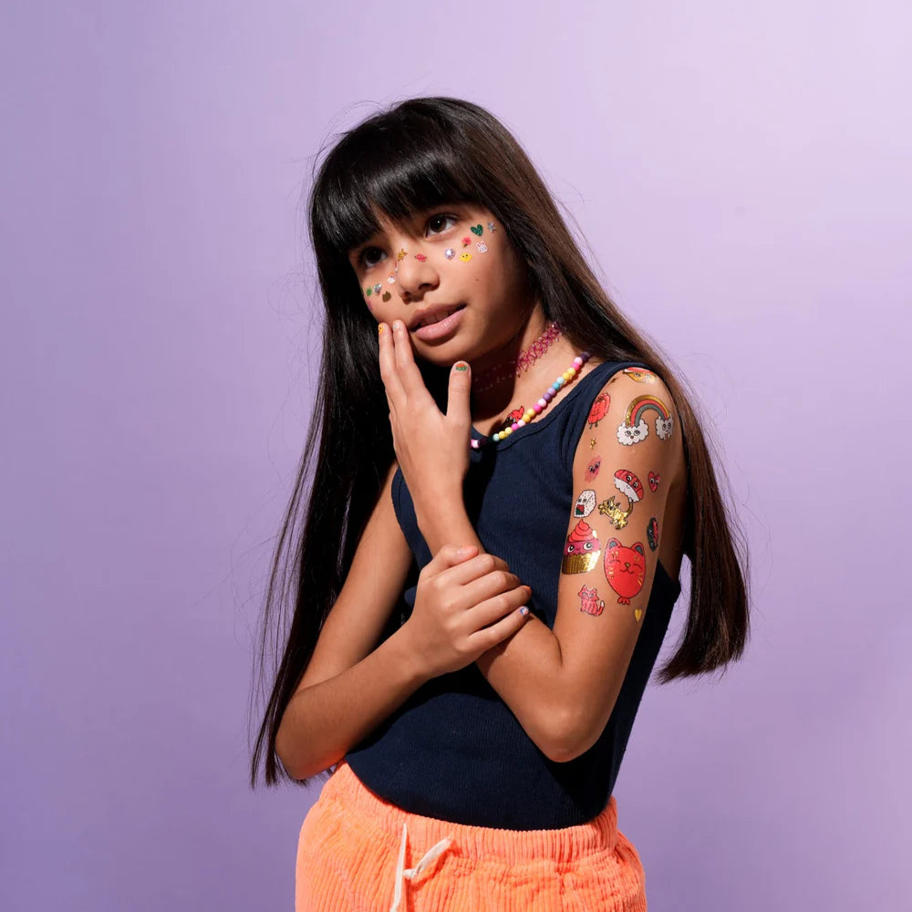 OMY Tattoos Kawaii: a girl in a navy top shows colorful temporary tattoos on her arm and face with a playful gaze.