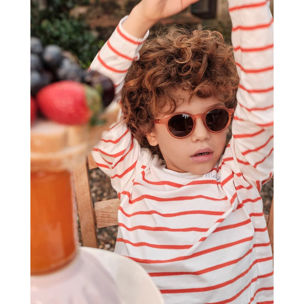 Child wearing red and white striped shirt and sunglasses with a fruit bowl in the background