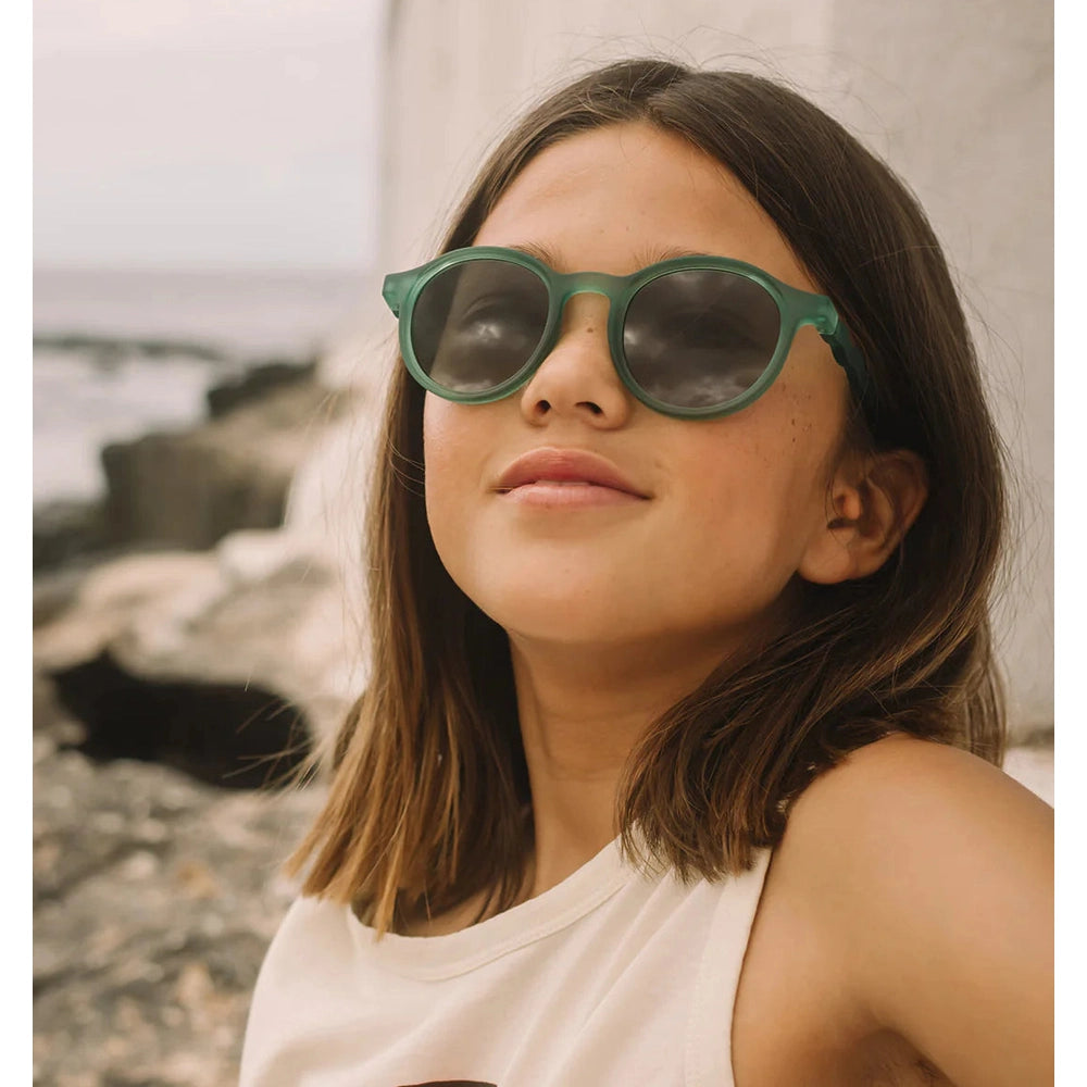 OLIVIO & CO Oval Sunglasses Junior+ Olive Green worn by a girl at the seaside