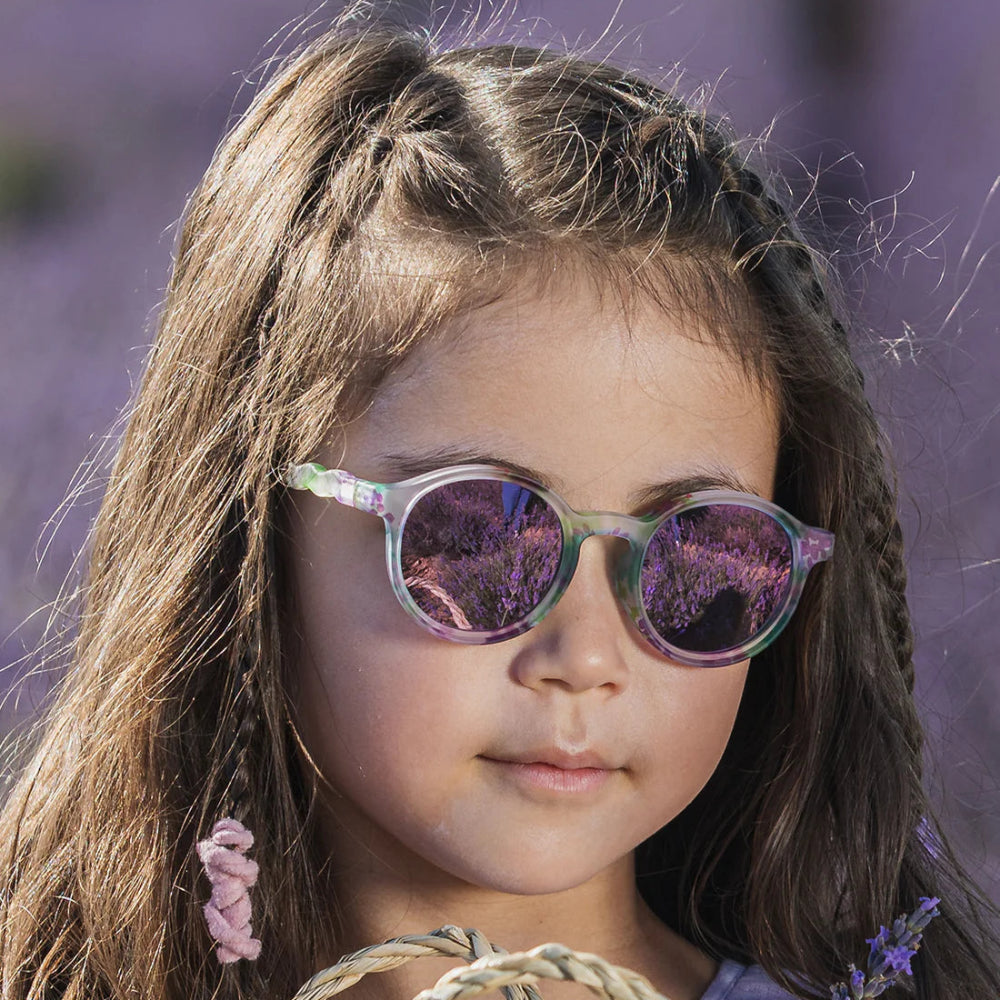 Olivio & Co Oval Sunglasses Kids/Junior Wild Flower: iridescent pastel frame with purple mirrored lenses, worn by a girl.