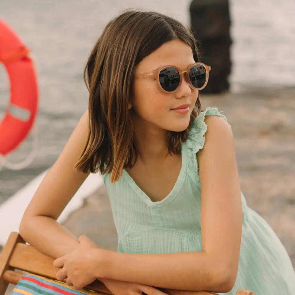 Olivio & Co Oval Sunglasses Junior+ Classic Olivio Sand Beige worn by a girl on a sunny dock with dark lenses