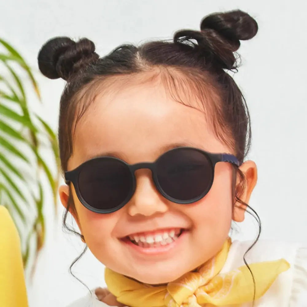 Olivio & Co Oval Sunglasses Kids/Junior Classic Olivio Squid Black worn by a smiling child in black rounded-oval frames.