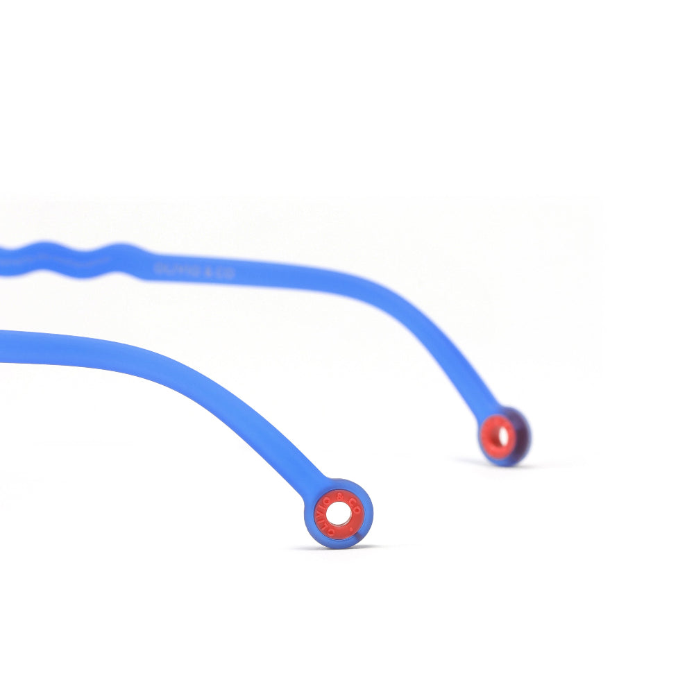 Olivio & Co Oval Sunglasses Kids/Junior Classic Olivio Chagall Blue resting on white surface, blue oval frames with red rims