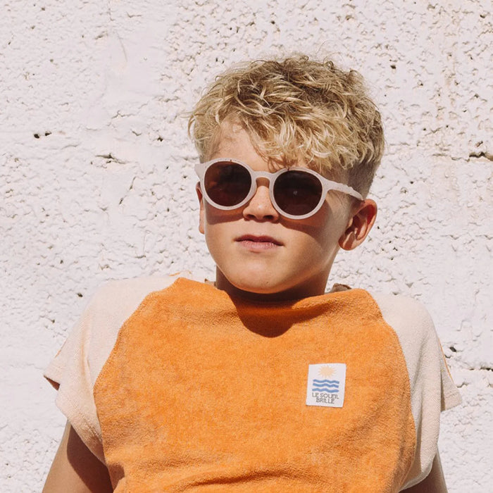 Olivio & Co Oval Sunglasses Kids/Junior Gelato Summer Vanilla Brownie on a kid wearing white-framed sunglasses with dark lenses against a white wall