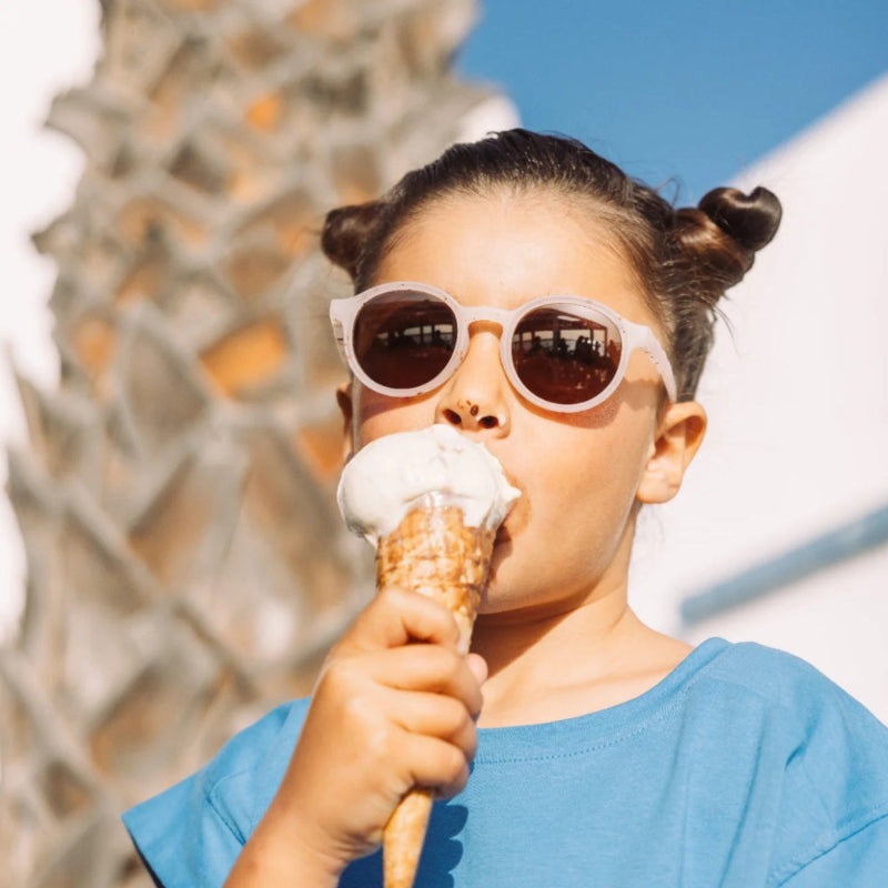 Olivio & Co Oval Sunglasses Kids/Junior Gelato Summer Vanilla Brownie, pink frames, brown lenses, worn by a girl enjoying ice cream.