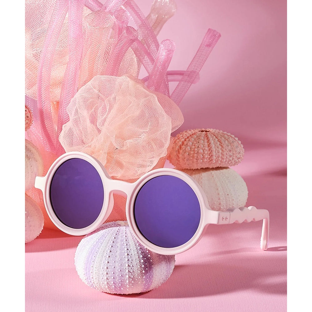 Olivio & Co Round Sunglasses Kids Coral Reef Coral Blush, white frame with purple lenses, placed beside pink seashells.