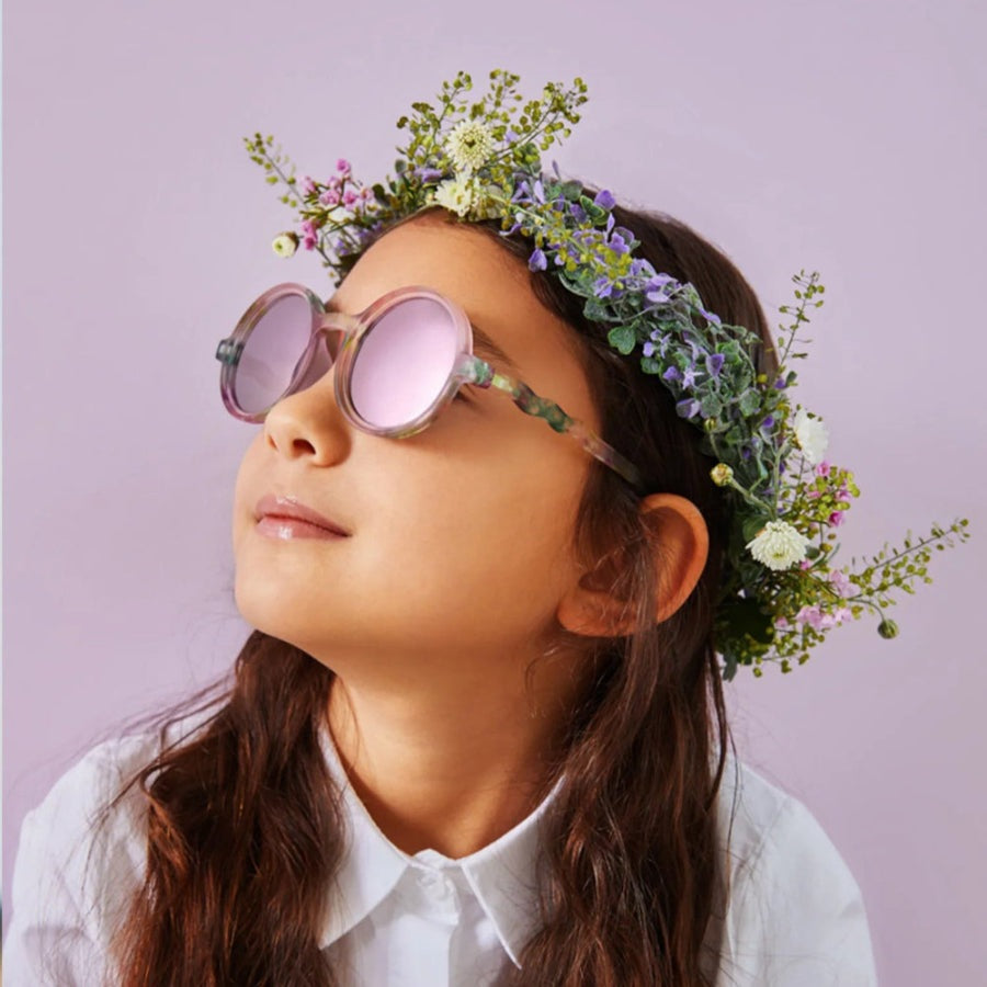 Olivio & Co Round Sunglasses for Kids with pink lenses and translucent frames, worn by a girl with a wildflower crown.