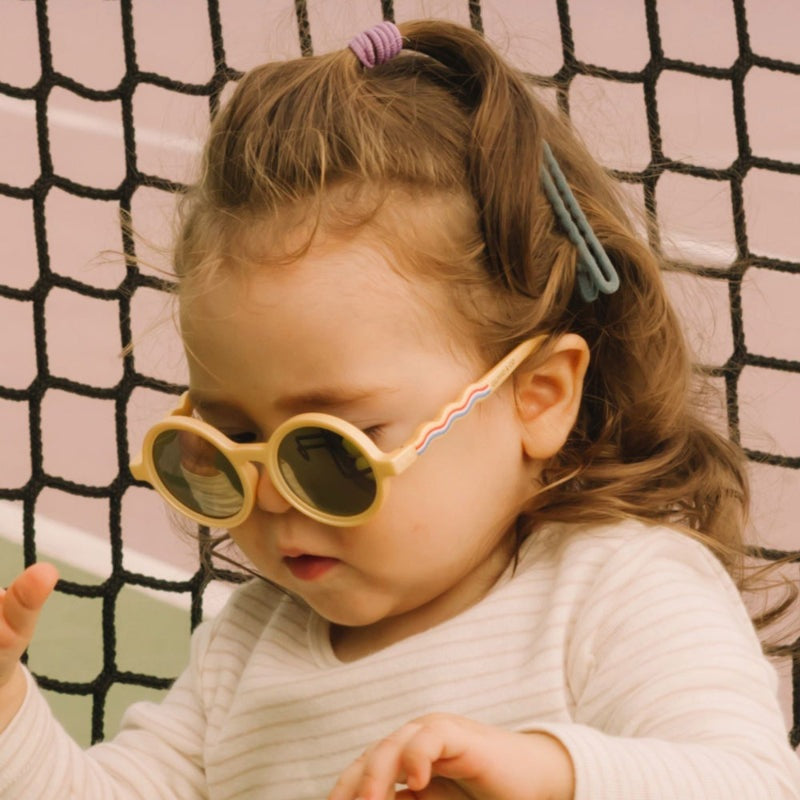 Olivio & Co Round Sunglasses Kids, medallion gold frames and cream temples, a girl wearing and adjusting them.