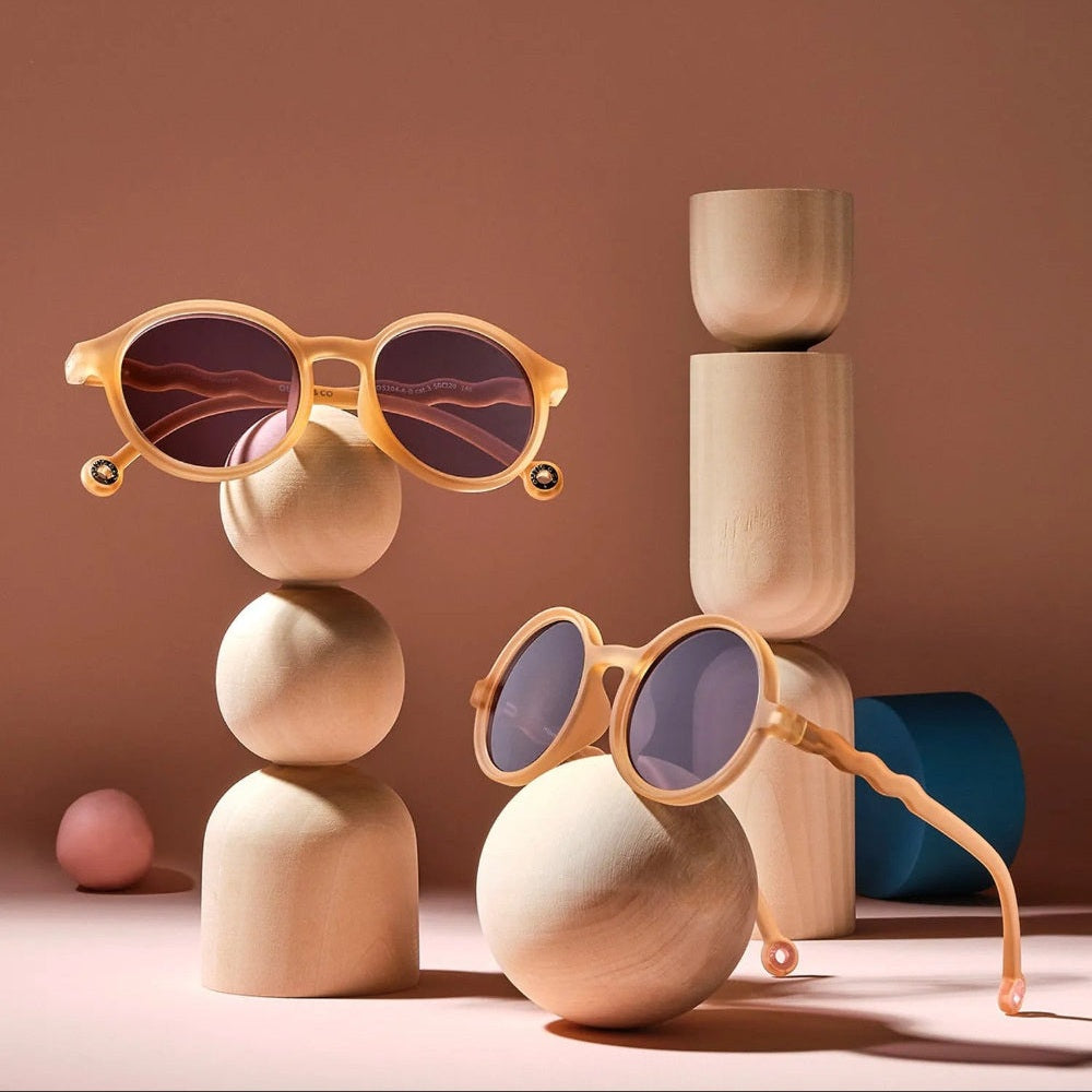 OLIVIO & CO Round Sunglasses Kids/Junior Classic in sand beige balanced on stacked wooden spheres.