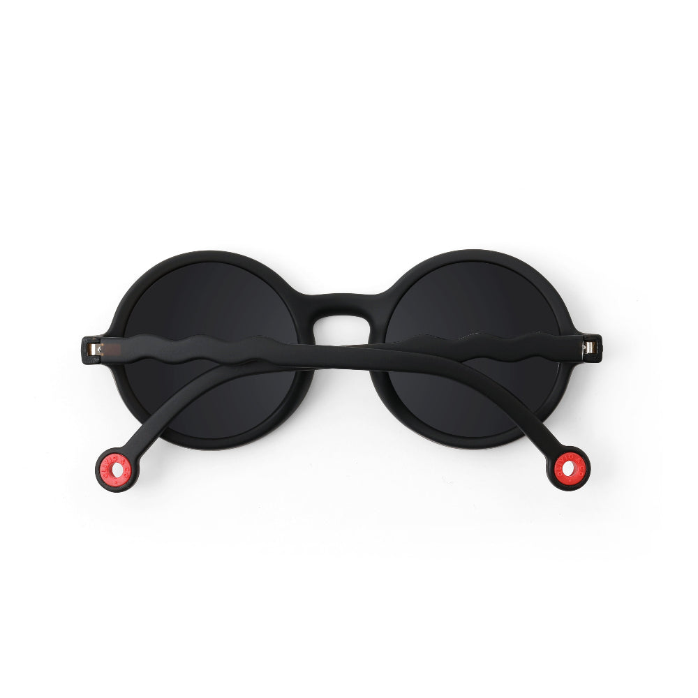Olivio & Co Round Sunglasses Kids/Junior Classic Olivio Squid Black, black frames with red hinge accents, arms resting across lenses.