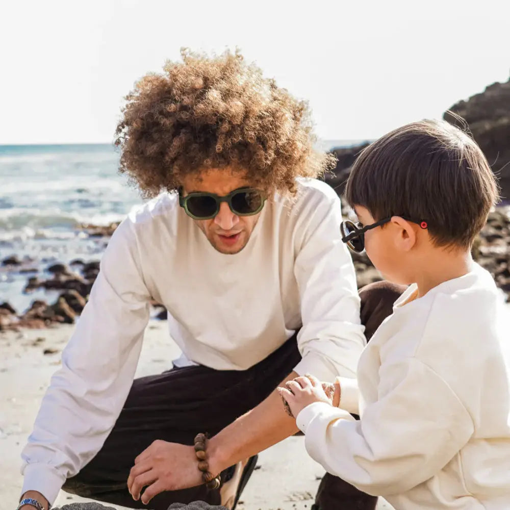 Olivio & Co Square Sunglasses Adult Creative Edition Olive Green worn by a man at the beach, shielding eyes with olive frames.