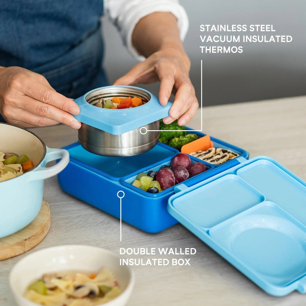 Omiebox Version 2 blue lunch box with stainless steel vacuum-insulated insert, as a parent fills the divided compartments with veggies.