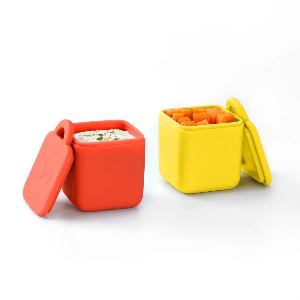Omielife Omiedip Sets lunch boxes, red and yellow silicone containers with lids, one filled with dip and diced carrots.