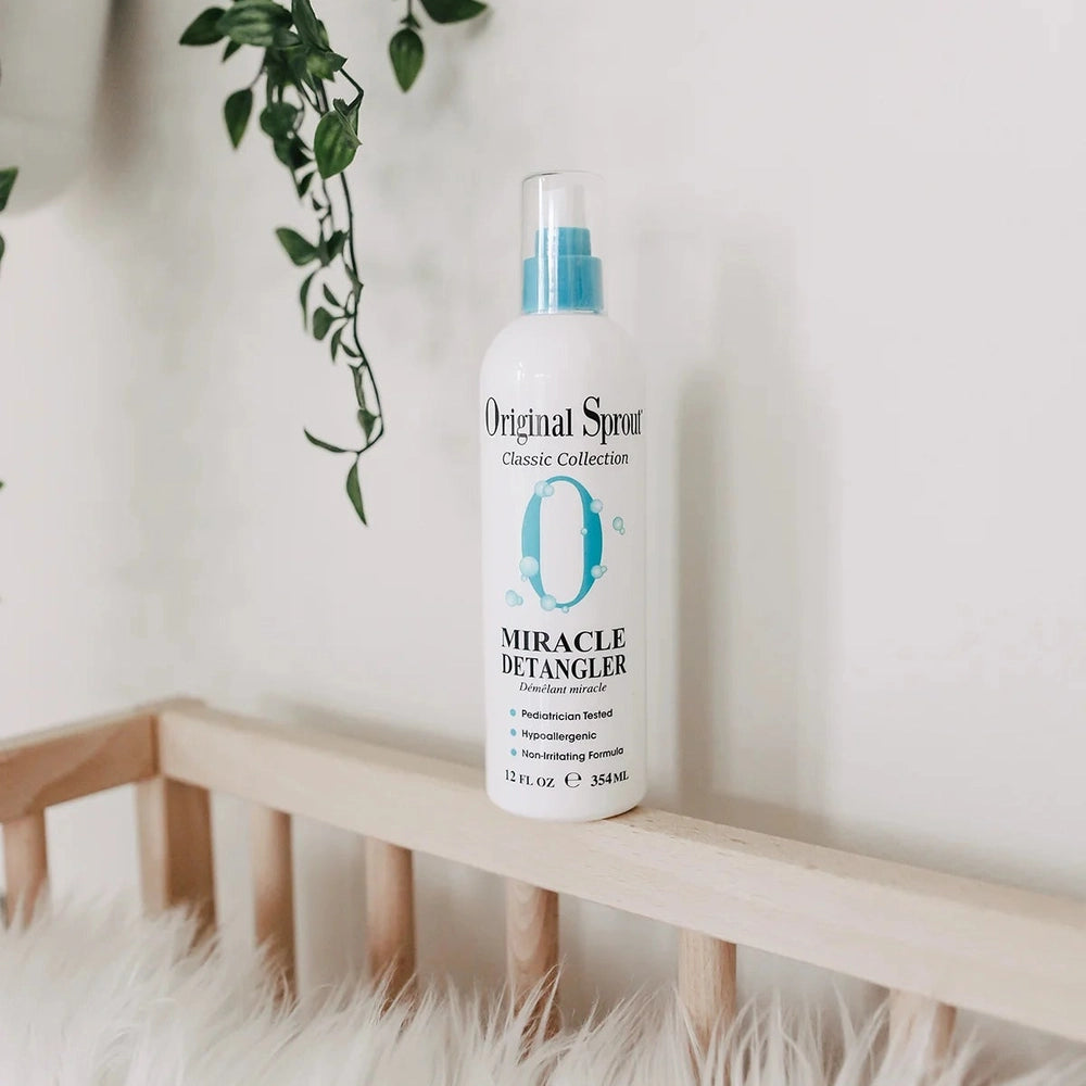 Original Sprout Miracle Detangler Spray 12 oz bottle with blue spray cap resting on a wooden railing beside hanging greenery
