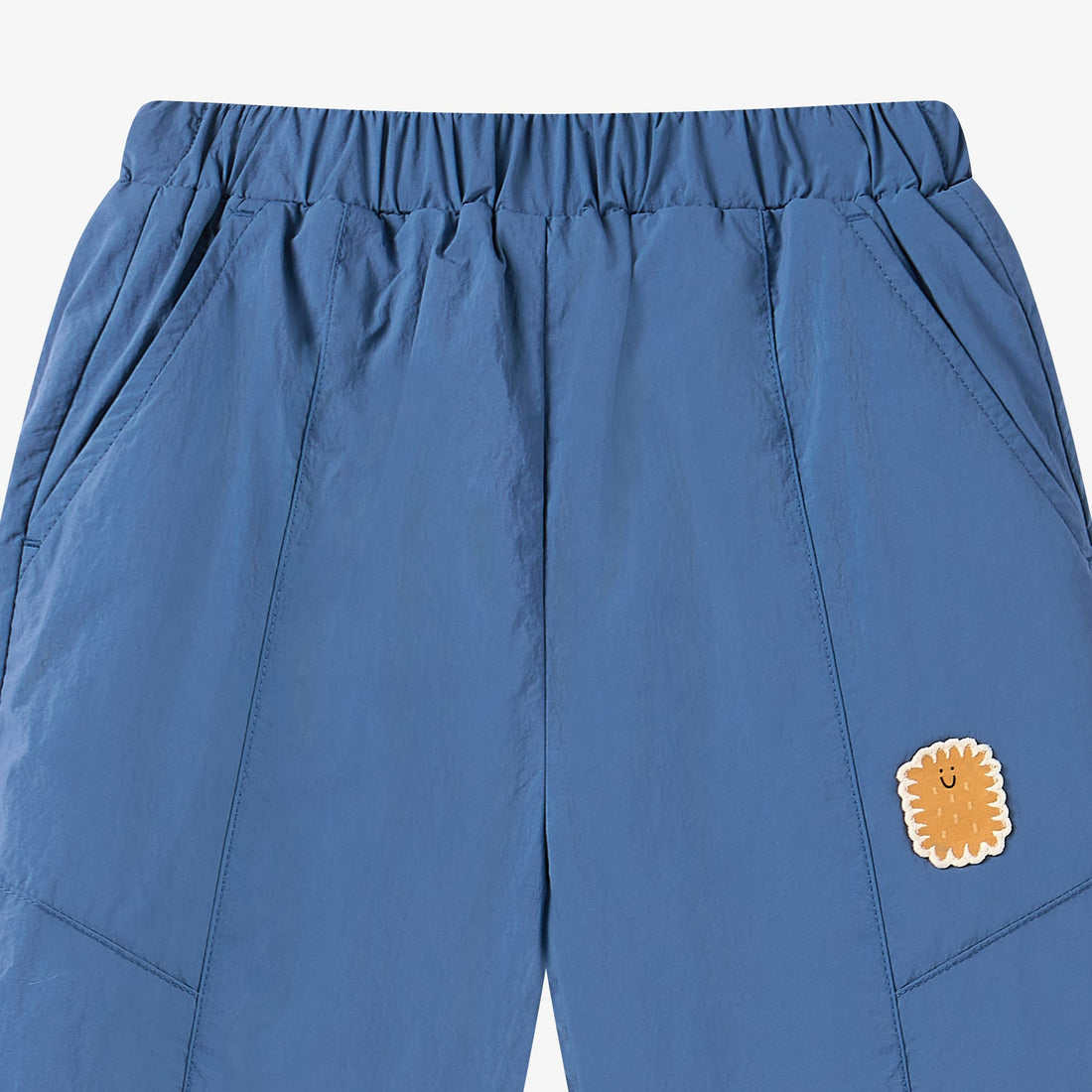 Nest Designs Biscuits & Vine Pants in Sea Blue, waist close-up with slanted pocket, panel seams, and golden character