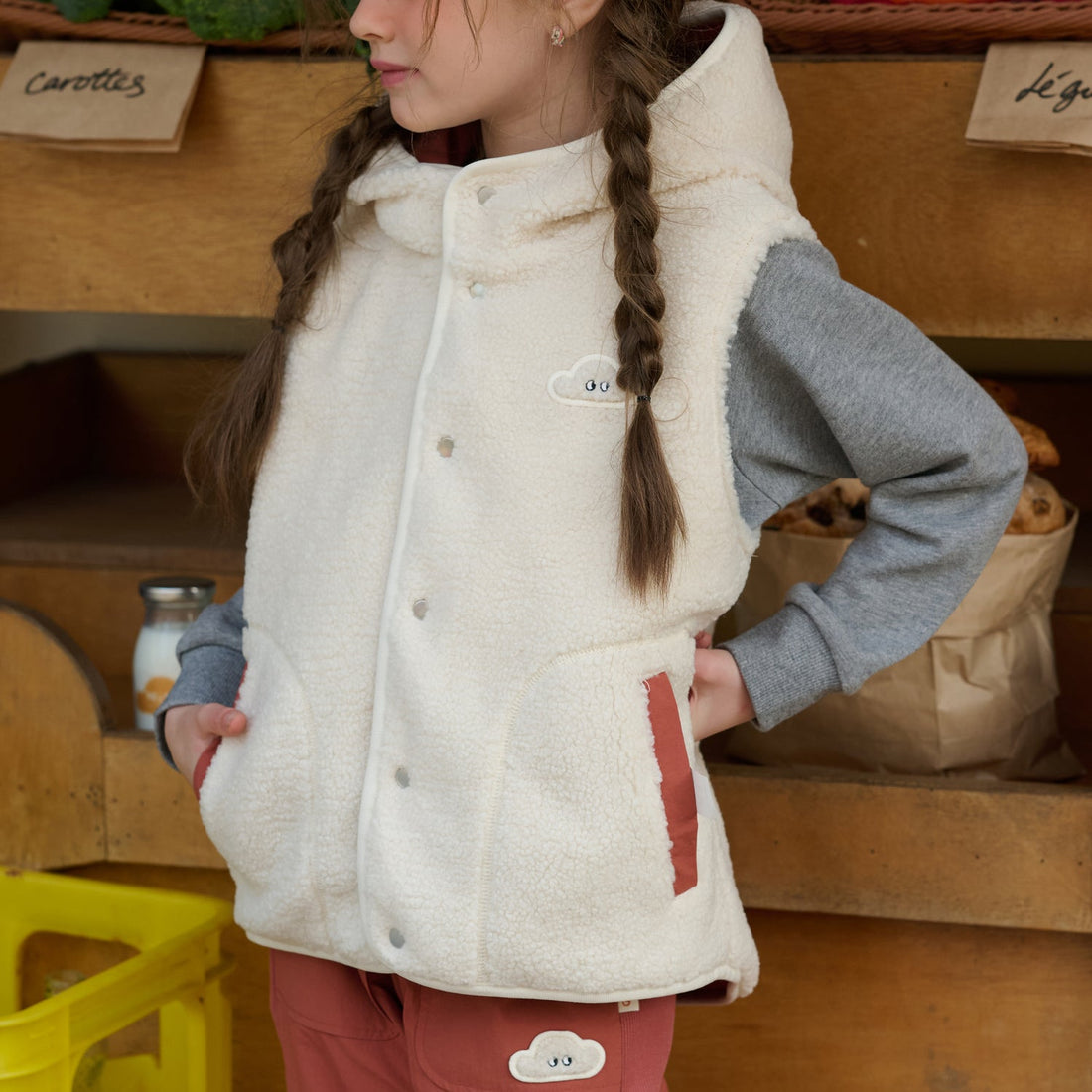 Nest Designs Cozy Crumbs Reversible Fleece Vest shown cream-fleece-side out with Redwood Burl pocket trim over a grey sweatshirt