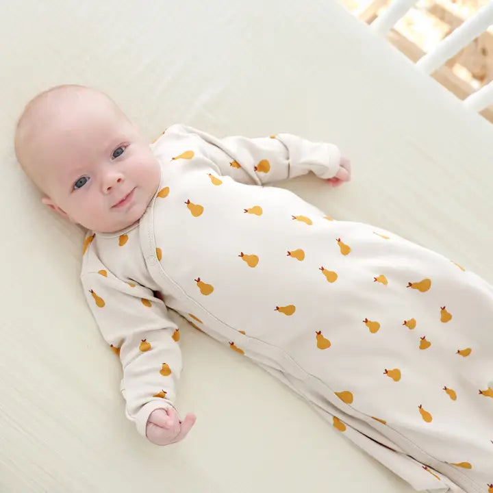 Parade Organic Gowns Signature Prints baby onesie in cream with yellow print, baby lying calmly on a bed.
