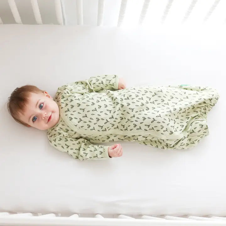 Parade Organic Gowns Signature Prints baby onesie in pale green with leaf pattern, baby calmly lying in a white crib.