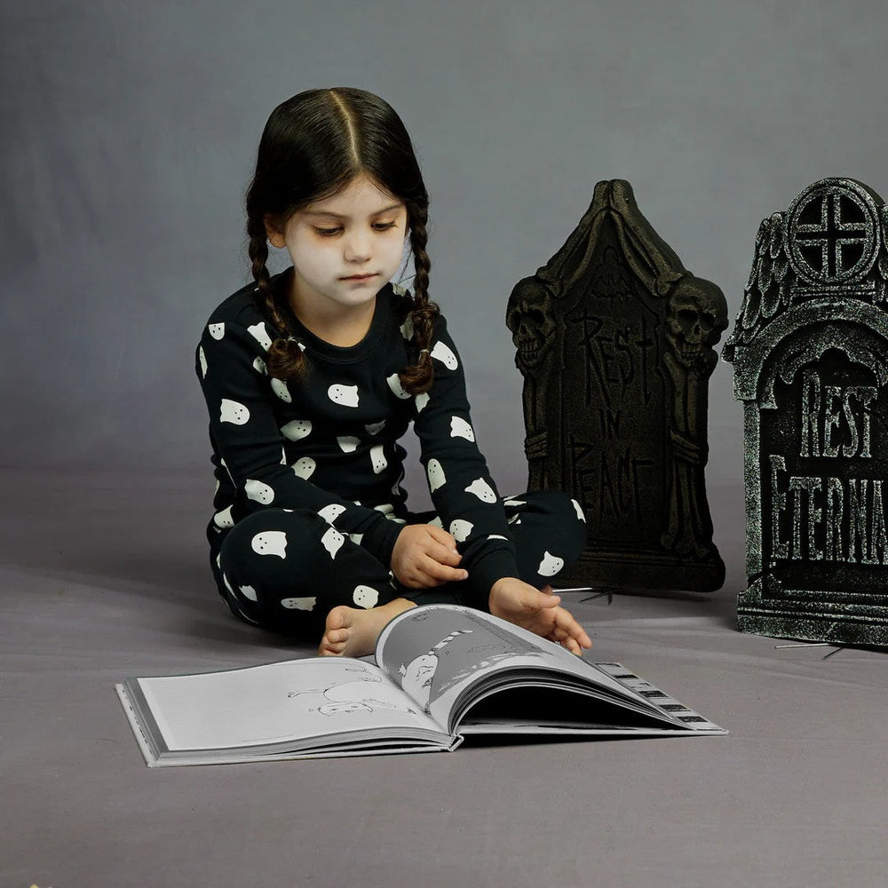 Petit Lem Ghosts Glow-In-The-Dark Print On Black Pajama Set: a girl in ghost-print black PJs sits reading a book.