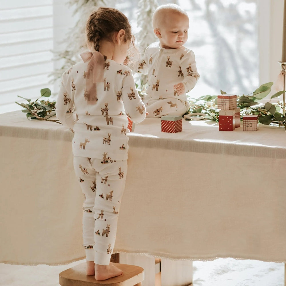 Petit Lem Rudy and Friends sleeper for babies; white knit with reindeer print, girl stands on stool inspecting blocks.