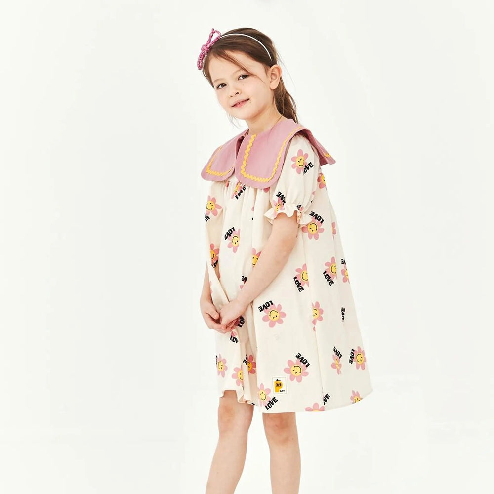 Petite Hailey Big Collar Dress Daisy Ivory; a girl posing in ivory dress with a pink oversized collar and yellow trim with daisies.